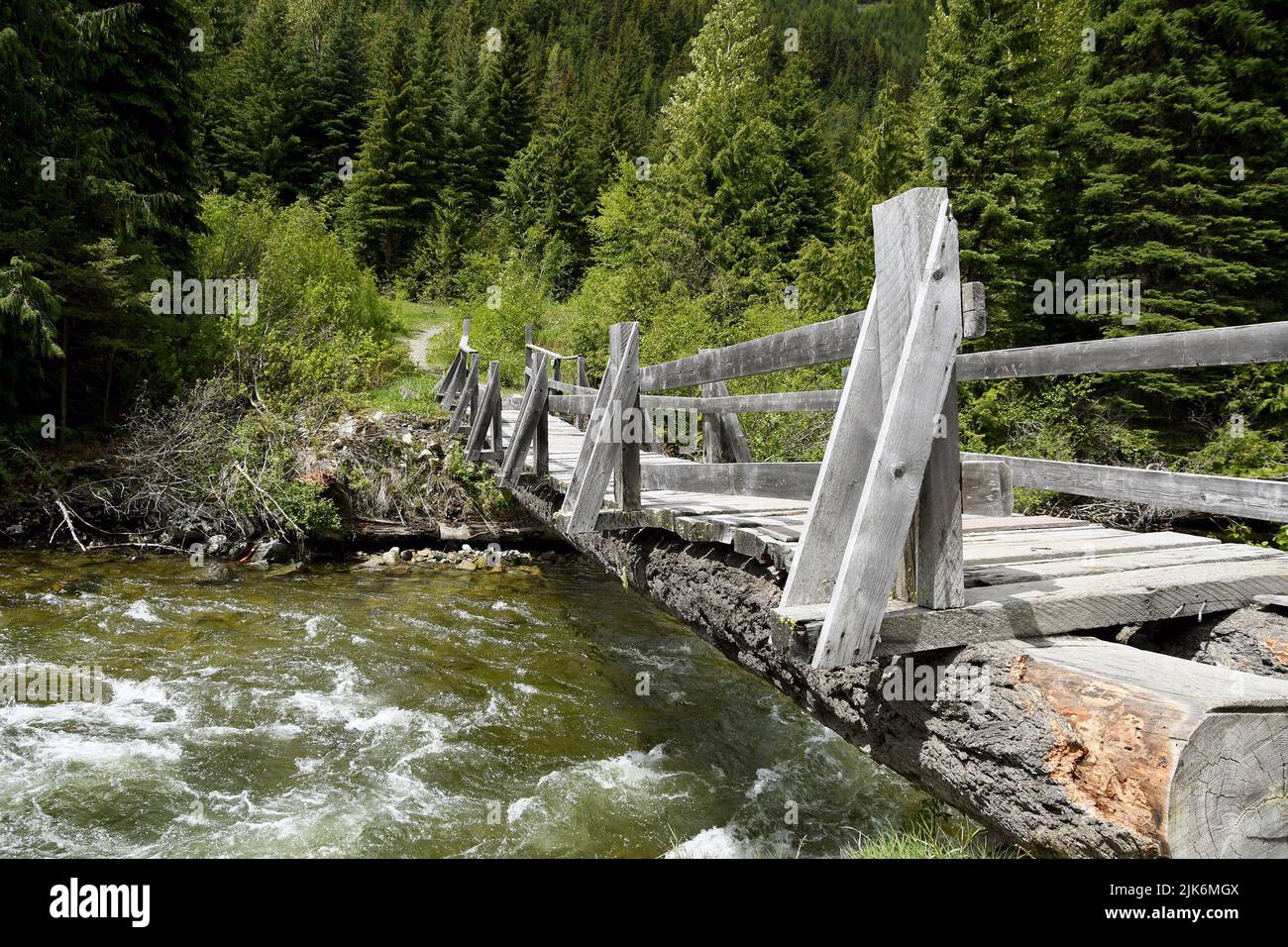 Puente hecho de madera talada a través de un pequeño río con agua clara. El camino conduce a un forerst. Ninguna gente. Foto de stock