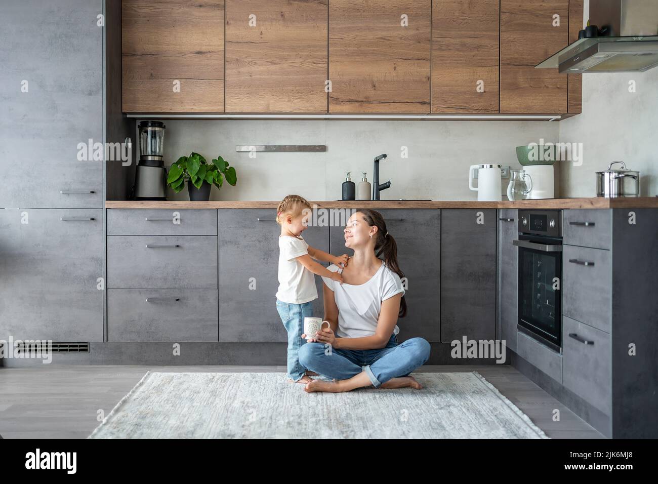 Niña y madre feliz con una taza de leche Diviértete en la cocina de casa Foto de stock
