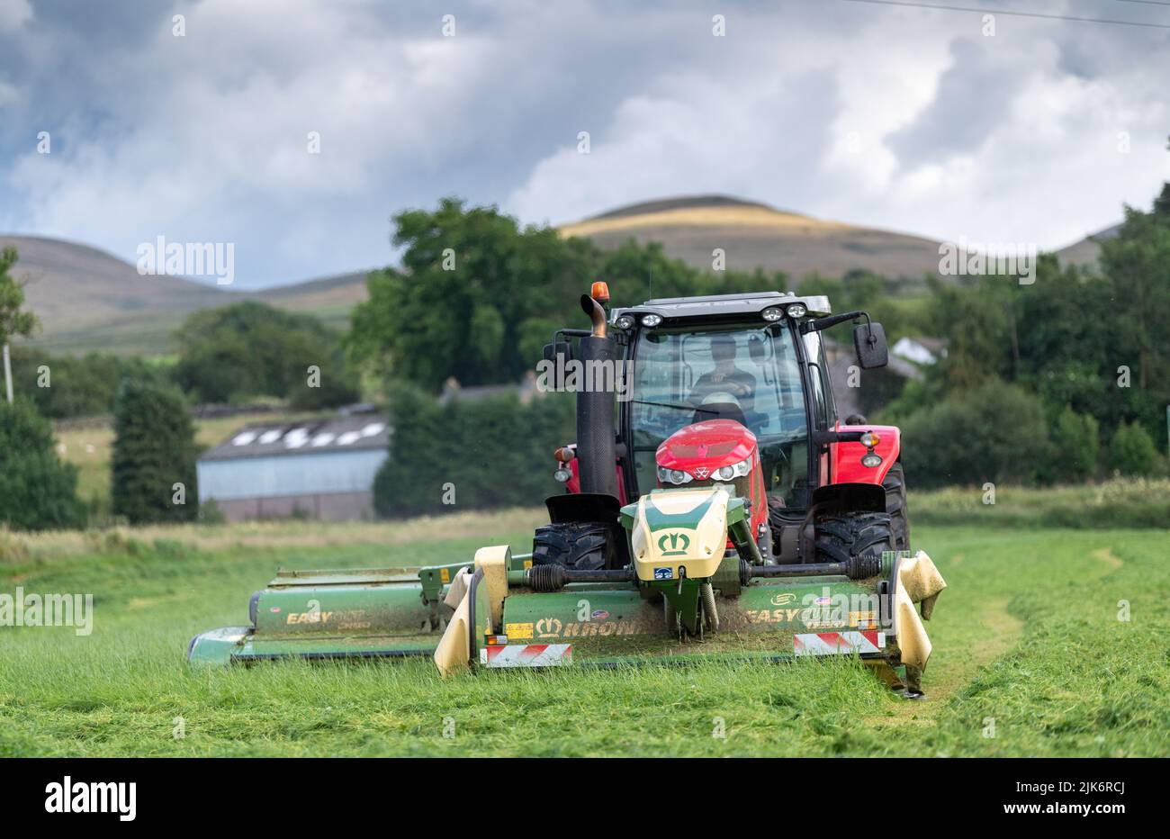 Segado de un prado para ensilado con un tractor Massey Ferguson 7718 y una combinación de segado Krone montado en la parte delantera y lateral. Cumbria, Reino Unido. Foto de stock