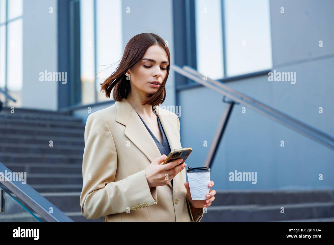 Una joven morena con el telón de fondo de un centro de negocios, centro de oficinas. Mientras se desplaza, lee las noticias desde su smartphone. Foto de stock
