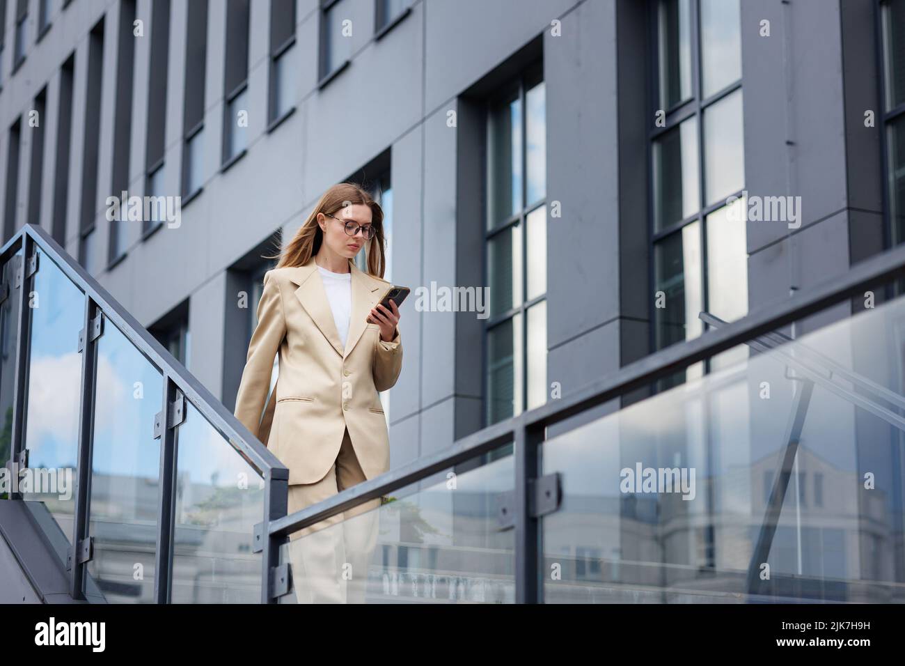 Una joven rubia contra el telón de fondo de un centro de negocios, centro de oficinas. Mientras se desplaza, lee las noticias desde su smartphone. Foto de stock