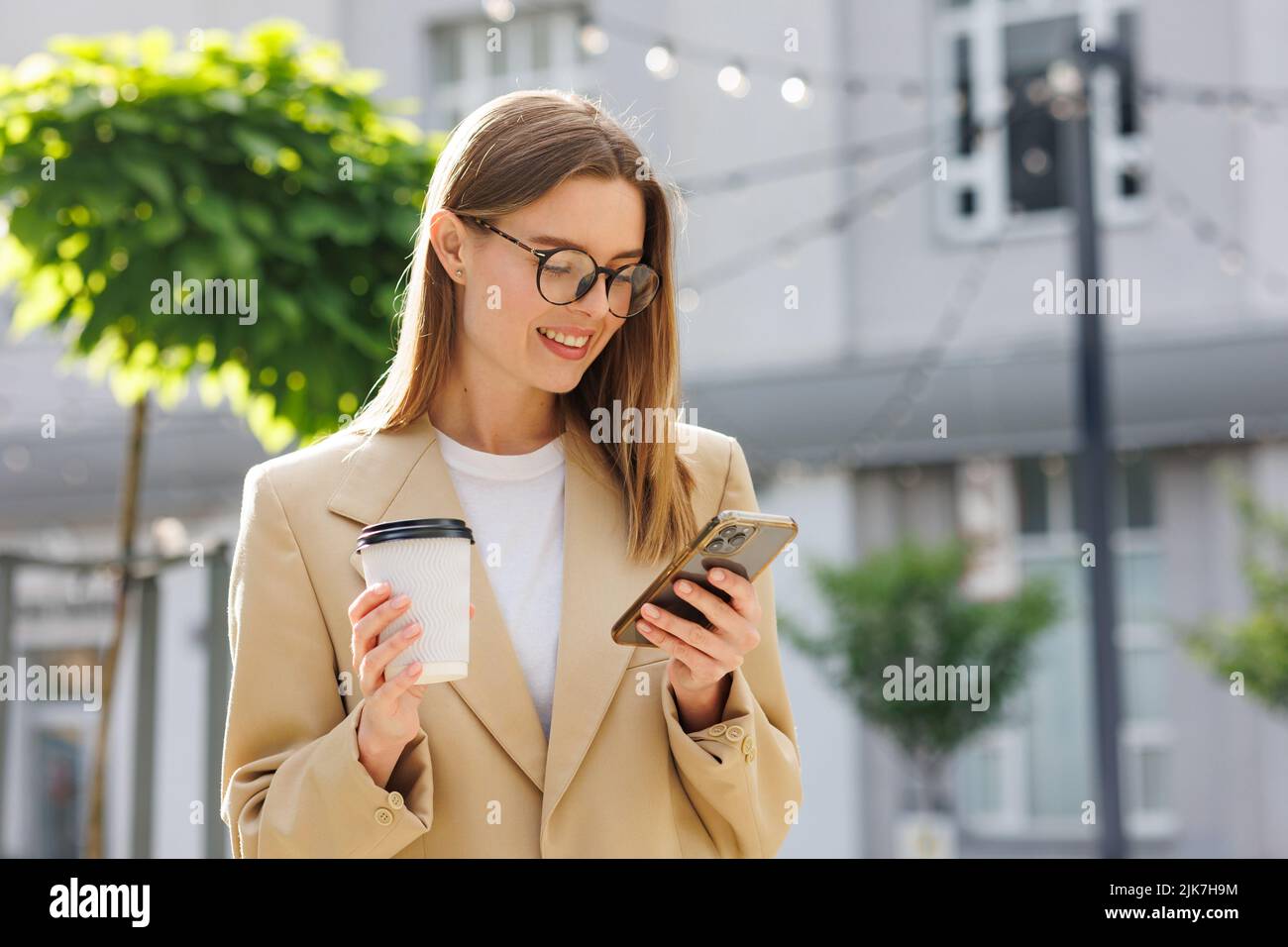Una joven rubia contra el telón de fondo de un centro de negocios, centro de oficinas. Retrato de un inicio correcto. Smartphone, café traje casual. Foto de stock