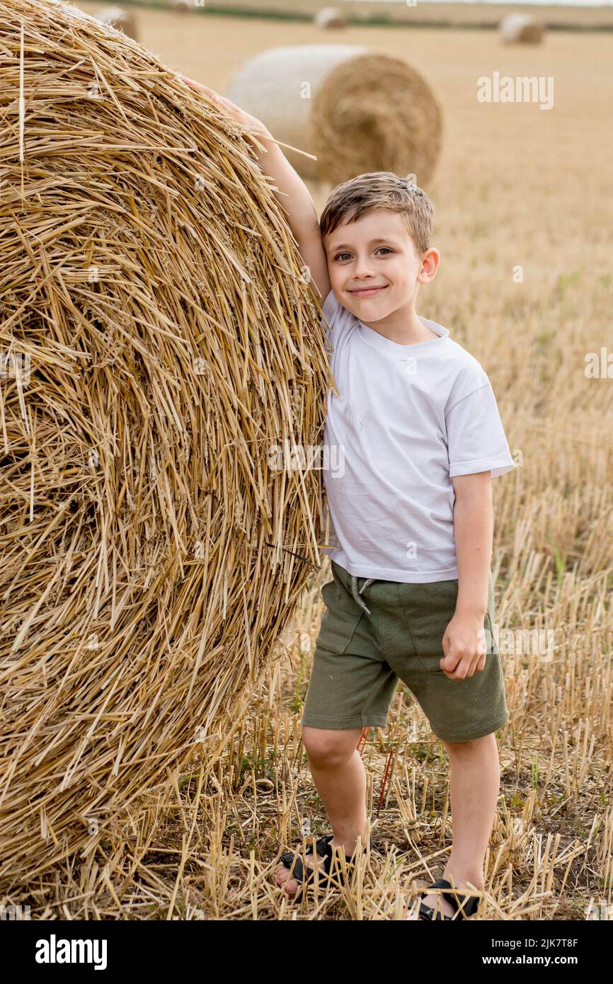 Un lindo niño en una blanca y pantalones cortos caqui está parado cerca de balas de heno redondas. Sesión de fotos en el campo Fotografía de stock - Alamy