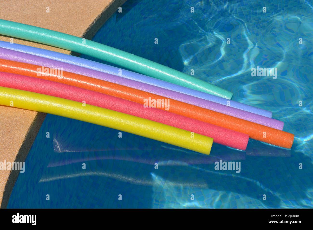 Vibraciones de verano. Fideos para nadar de color arco iris flotando al lado de la piscina Foto de stock