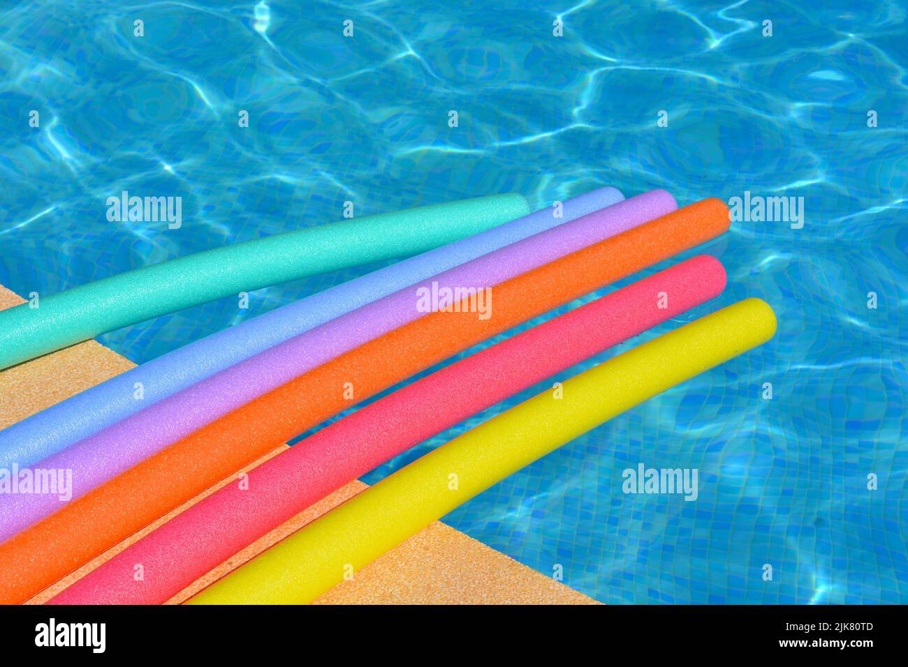 Vibraciones de verano. Fideos para nadar de color arco iris flotando al lado de la piscina Foto de stock
