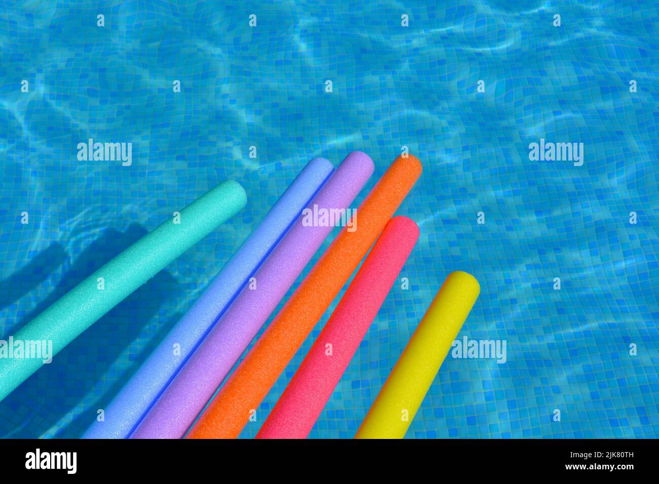 Fideos para nadar de color arco iris flotando en el agua de la piscina. Diversión veraniega Foto de stock
