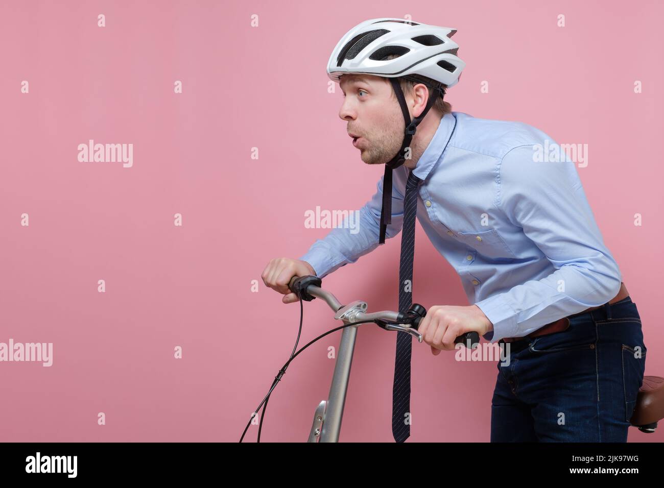 Hombre caucásico sorprendido con casco en bicicleta sobre fondo rosa Foto de stock