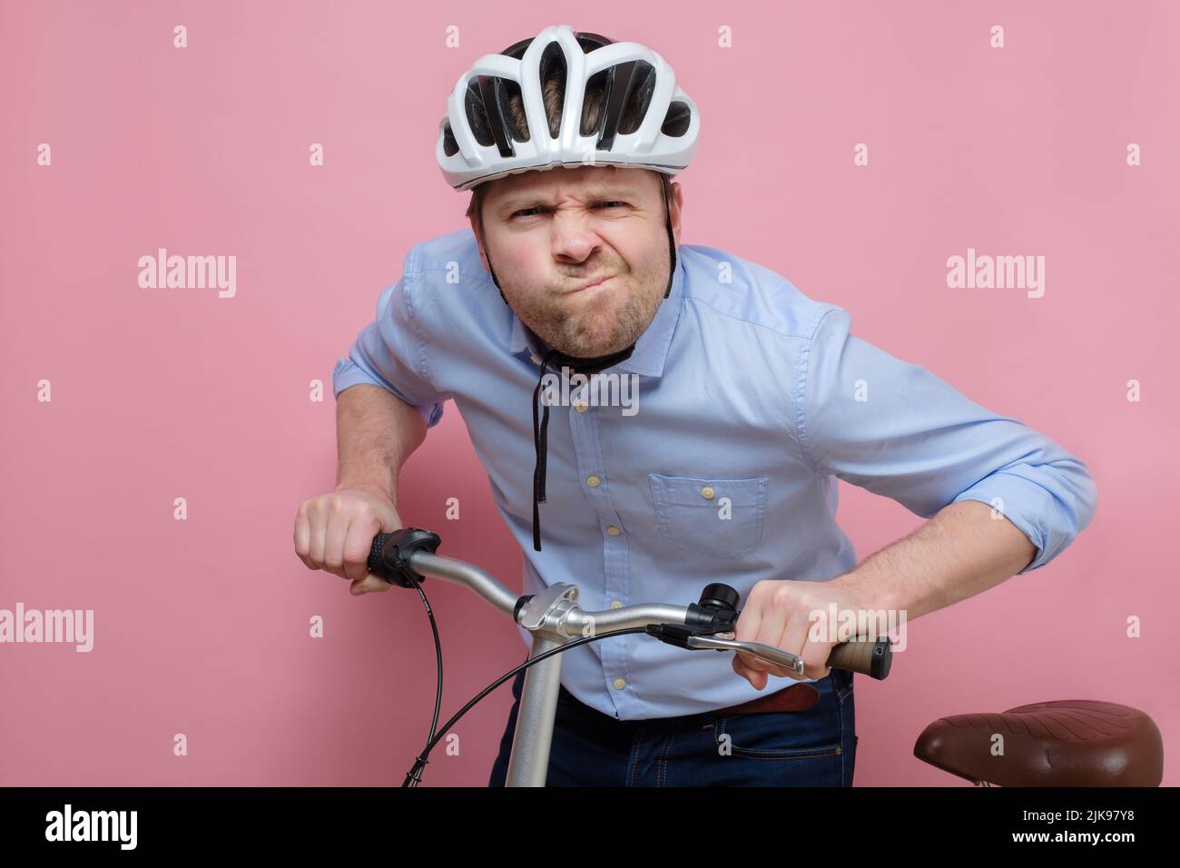Hombre caucásico confundido que lleva en bicicleta sobre fondo rosa Foto de stock