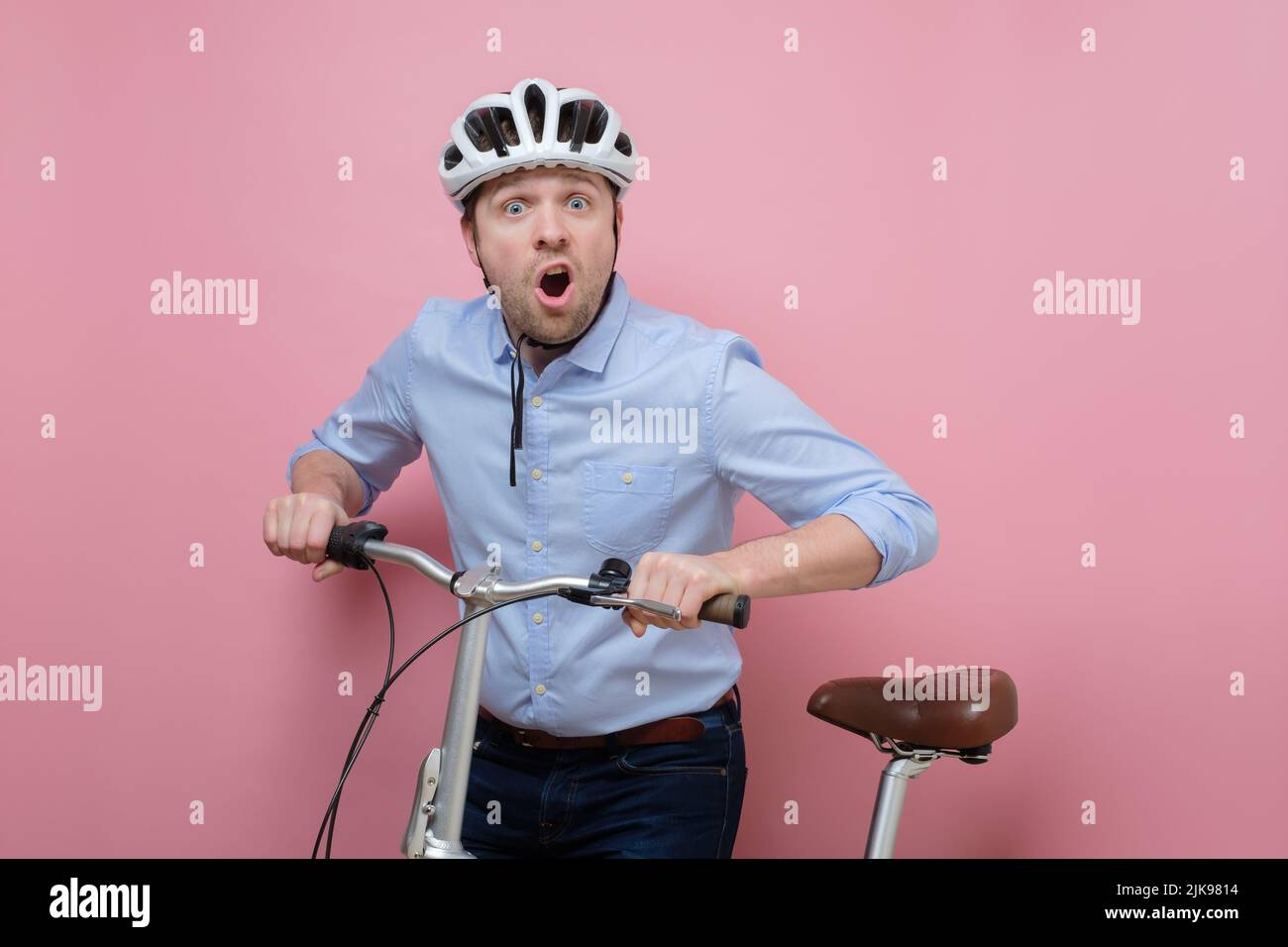 Hombre caucásico sorprendido con casco en bicicleta sobre fondo rosa Foto de stock