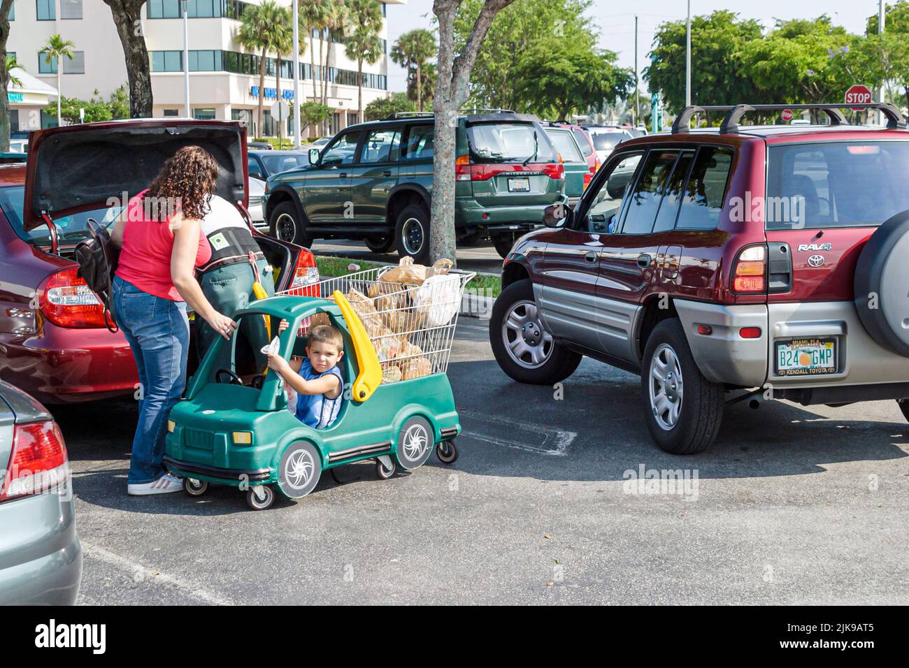 Miami Florida, shopper center centro comercial estacionamiento estacionamiento estacionamiento estacionamiento, mujer hispana madre agarrando niño hijo carro como el vehículo de las copias de seguridad prevención de accidentes Foto de stock