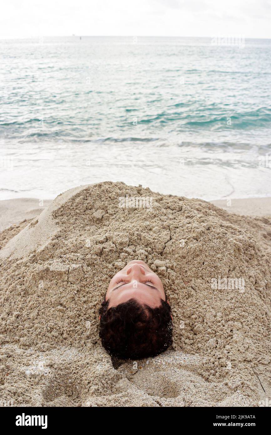 Miami Beach Florida, Atlantic Ocean Shore, costa a la orilla del mar, hombre hispano, arena enterrada por el surf en el agua, adolescente adolescente Foto de stock