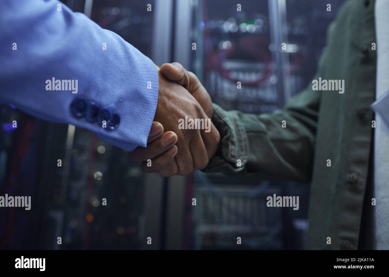 Me complace ayudar. Dos irreconocibles agentes masculinos de soporte DE TI se dan la mano en una sala oscura de servidores de red. Foto de stock