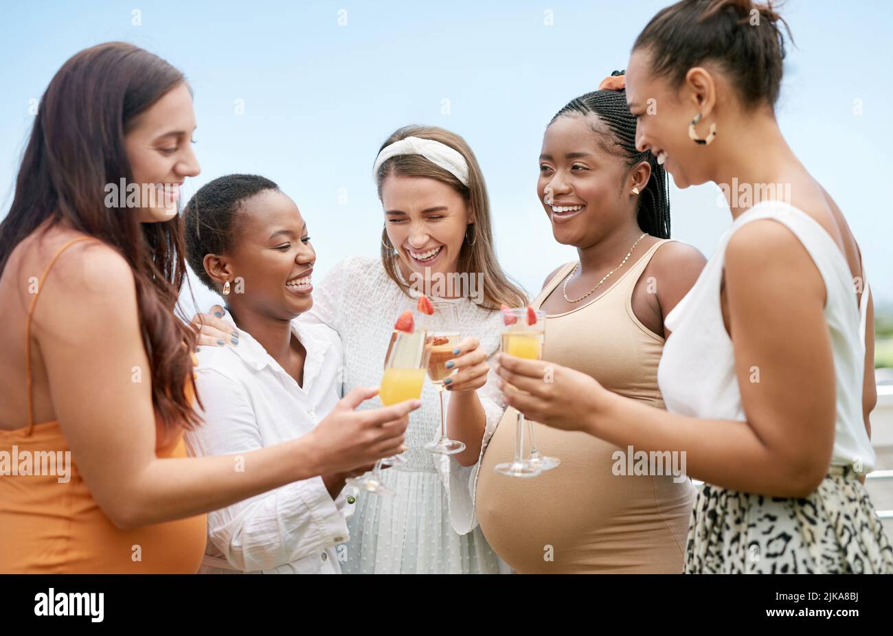 Saludos a usted y a su pequeña. Un grupo de amigas que toastan a su amiga embarazada en una ducha del bebé. Foto de stock
