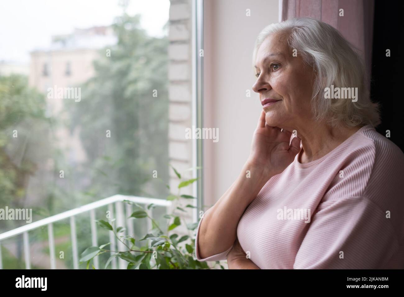 Sonriendo anciana mujer caucásica mira por la ventana. Foto de stock