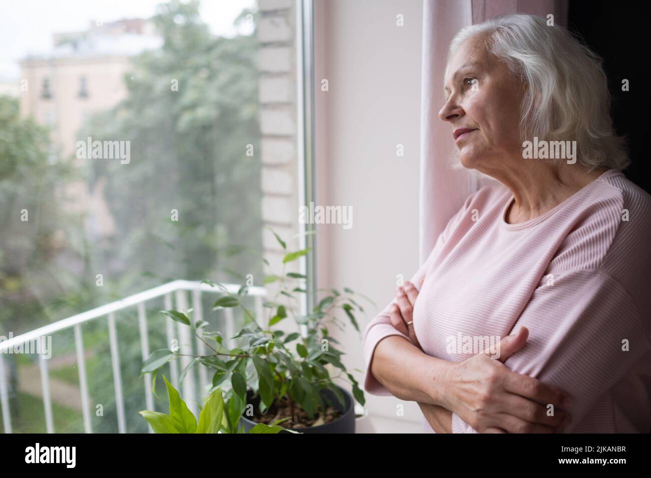 Una anciana mujer caucásica mira tristemente por la ventana. Foto de stock