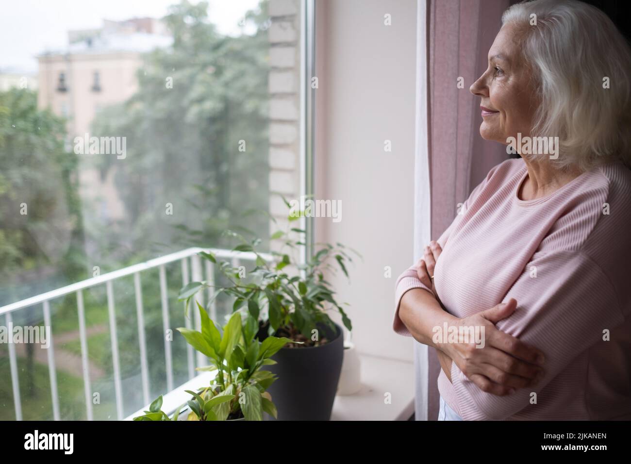 Sonriendo anciana mujer caucásica mira por la ventana. Foto de stock