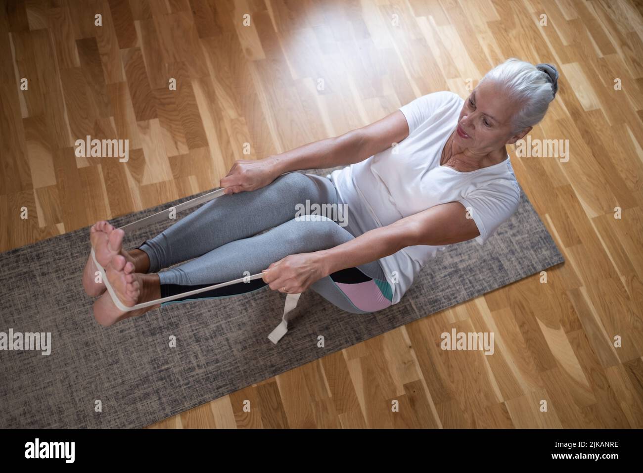 Mujer caucásica mayor haciendo ejercicios de abs, sentado en barco yoga pose en casa. Yoga a la vejez. Foto de stock
