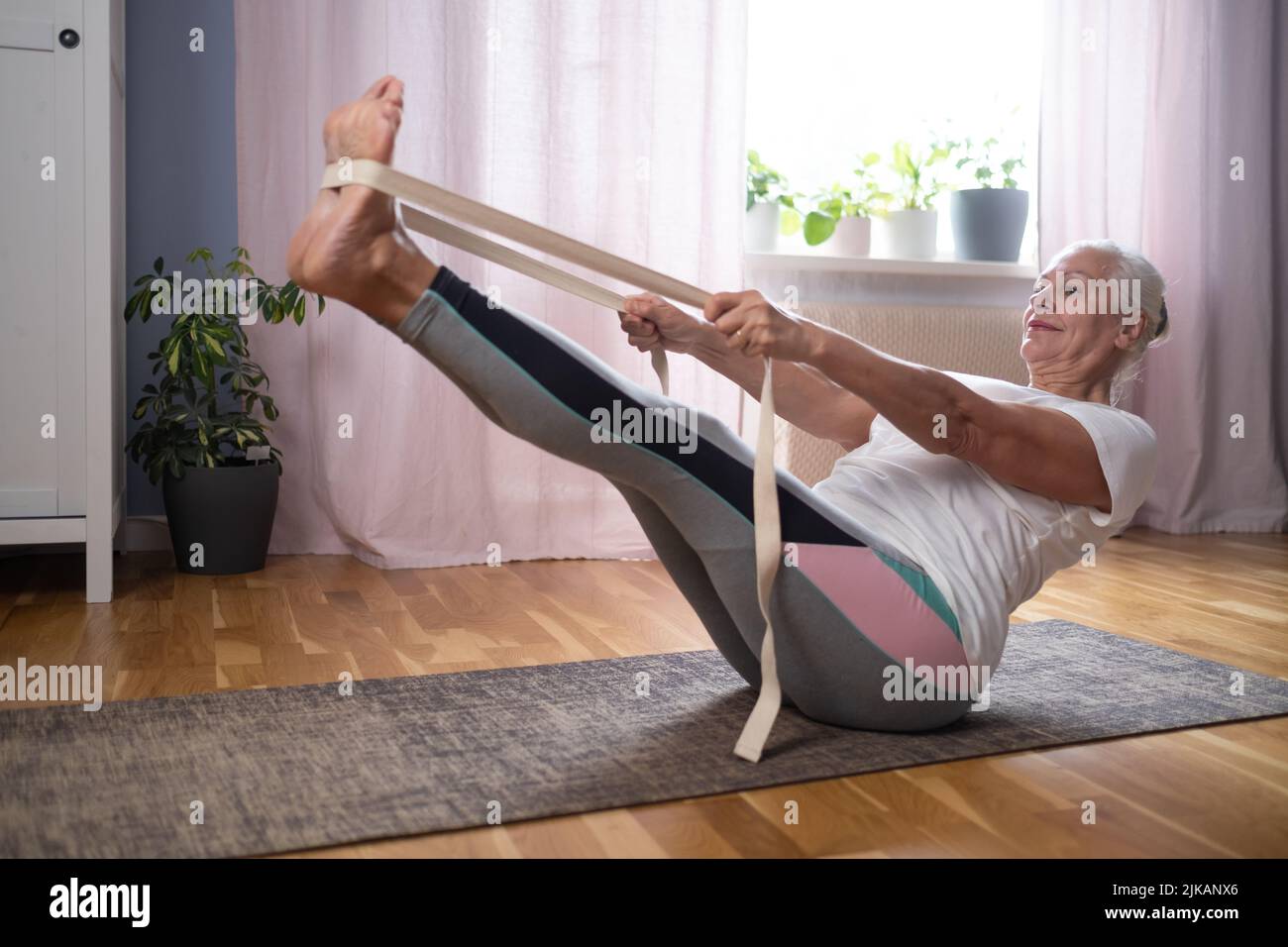 Mujer caucásica mayor haciendo ejercicios de abs, sentado en barco yoga pose en casa. Yoga a la vejez. Foto de stock