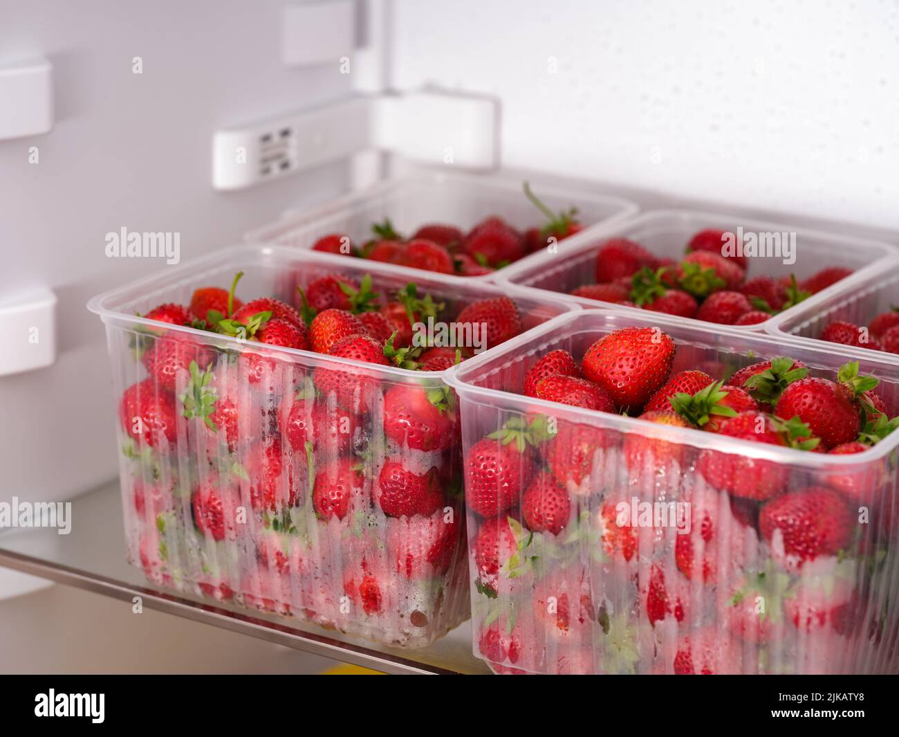 Grandes contenedores de plástico con fresas rojas orgánicas en la nevera Foto de stock