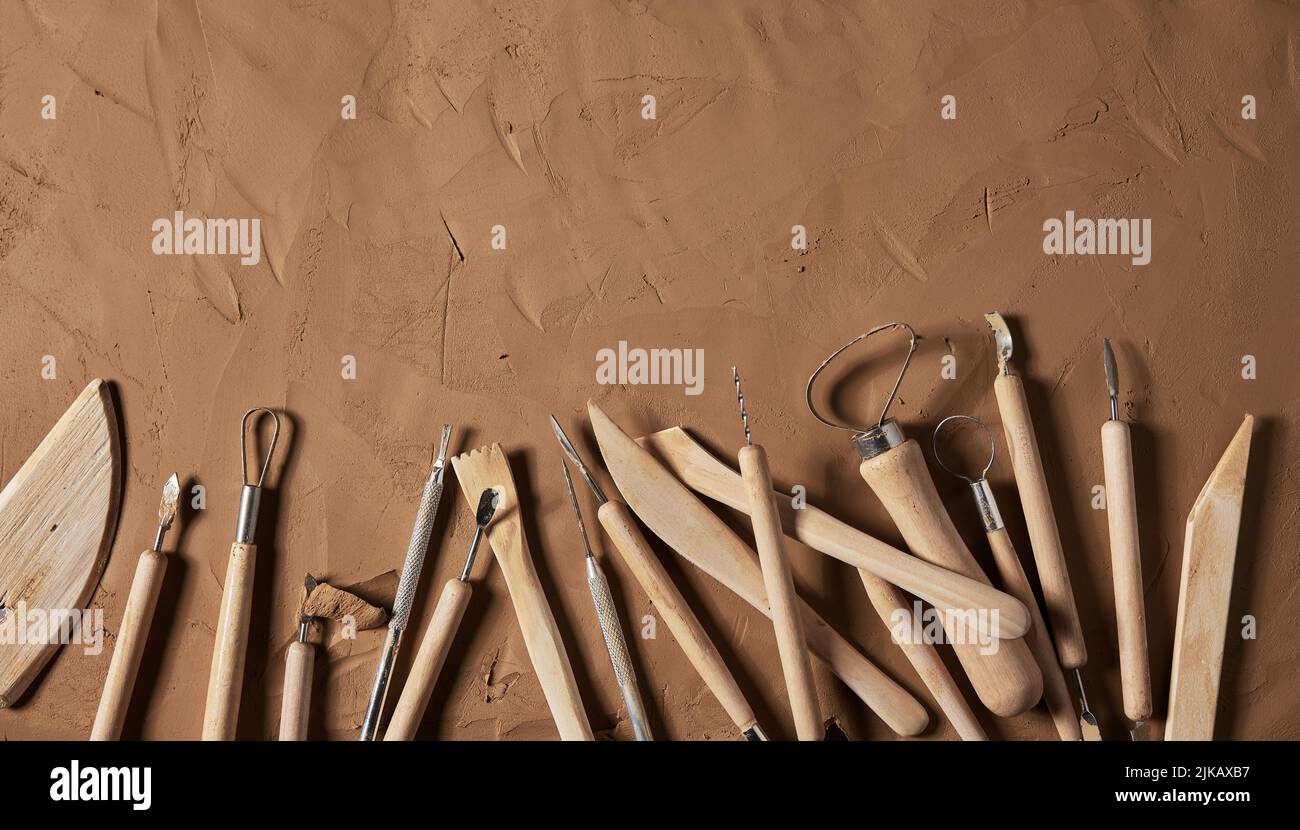 Vista superior de varias herramientas con mangos de madera para modelar cerámica colocada sobre fondo de arcilla marrón en estudio de luz Foto de stock