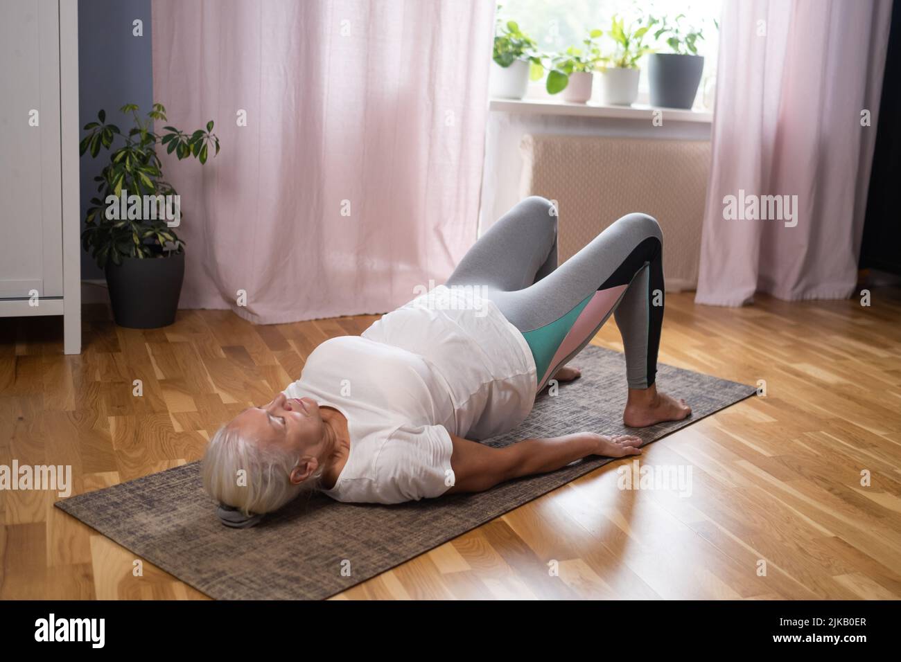 Mujer de yoga atlética mayor haciendo ardha chakrasana rueda en la estera de yoga en casa. Yoga para personas mayores concepto Foto de stock