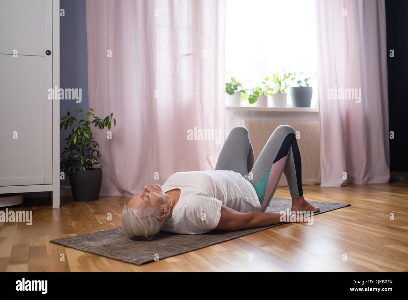 Mujer de yoga atlética mayor haciendo ardha chakrasana rueda en la estera de yoga en casa. Yoga para personas mayores concepto Foto de stock