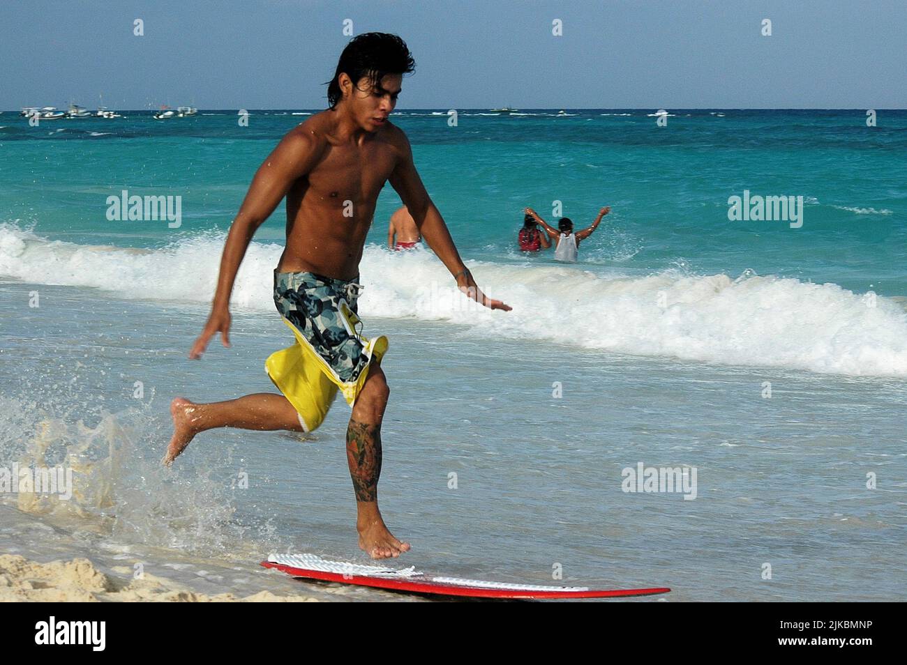 Un joven jugando con una tabla de surf en la playa en un día de verano en Playa del Carmen, México. Enfoque selectivo Foto de stock