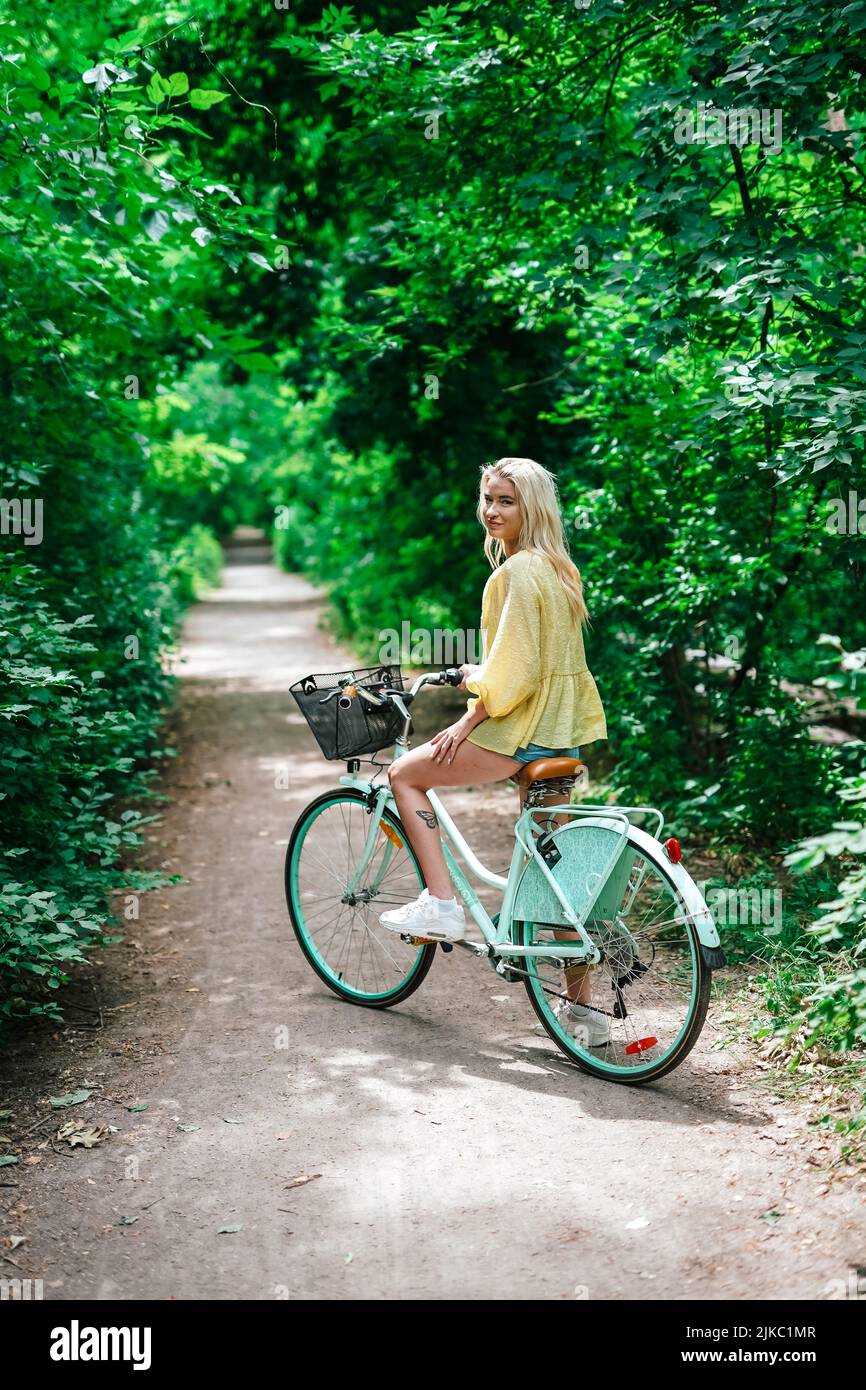 joven rubia a punto de montar una bicicleta en un sendero de verano fuera Foto de stock