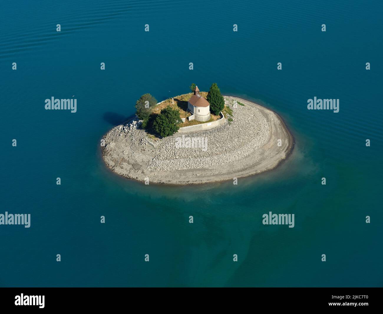 VISTA AÉREA. Capilla en una isla rodeada de aguas turquesas. Isla de Saint-Michel, Prunières, Lago Serre-Ponçon, Altos Alpes, Francia. Foto de stock