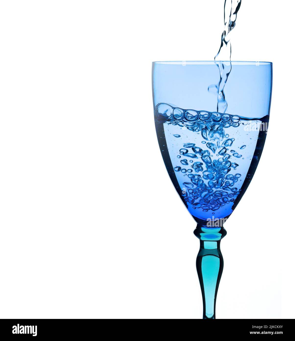 Agua que se vierte en vidrio azul y turquesa, aislada sobre fondo blanco. Refresco en el calor. No hay hielo. Foto de stock