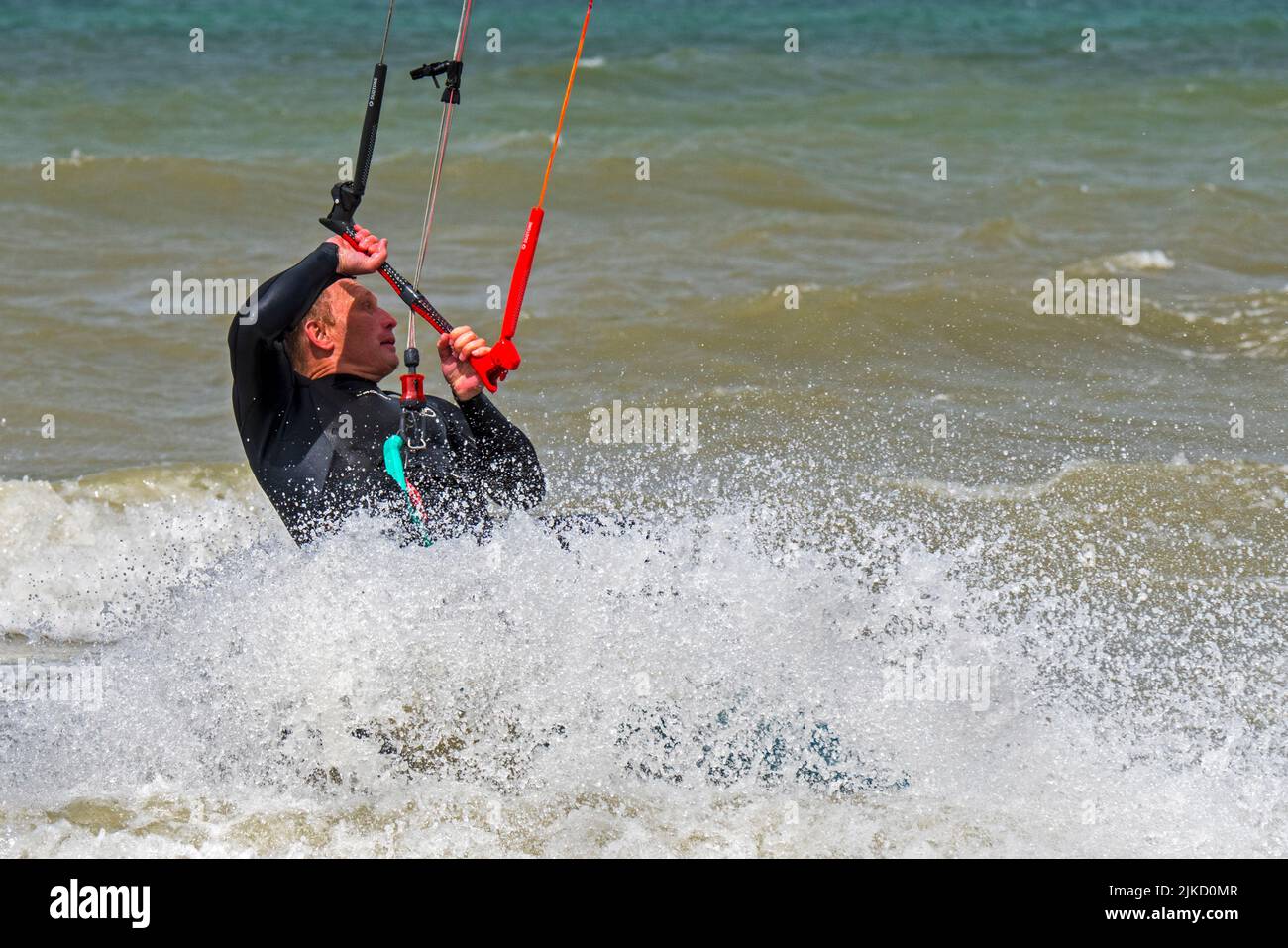 Kiteboarder / kitesurfer con traje de neopreno sobre tabla de twintip kitesurfing en el Mar del Norte Foto de stock