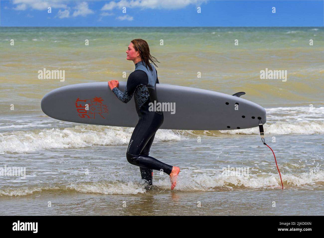Mujer joven surfista en la playa corriendo con tabla de surf en el mar para ir a surfear Foto de stock