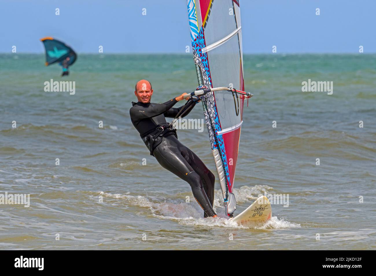 Windsurfista recreativo en traje negro practicando windsurf clásico a lo largo de la costa del Mar del Norte Foto de stock