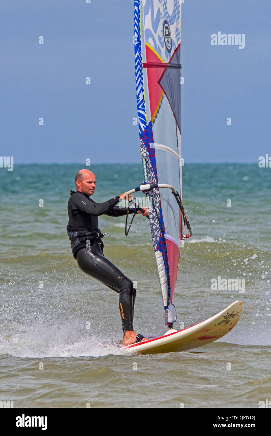 Windsurfista recreativo en traje negro practicando windsurf clásico a lo largo de la costa del Mar del Norte Foto de stock