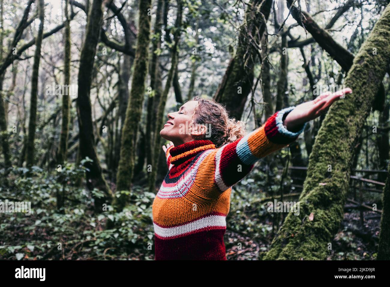 Mujer adulta feliz sonríe y abre los brazos para abrazar el hermoso bosque natural a su alrededor. Concepto de ambiente verde y turismo sostenible gente de viaje. Foto de stock