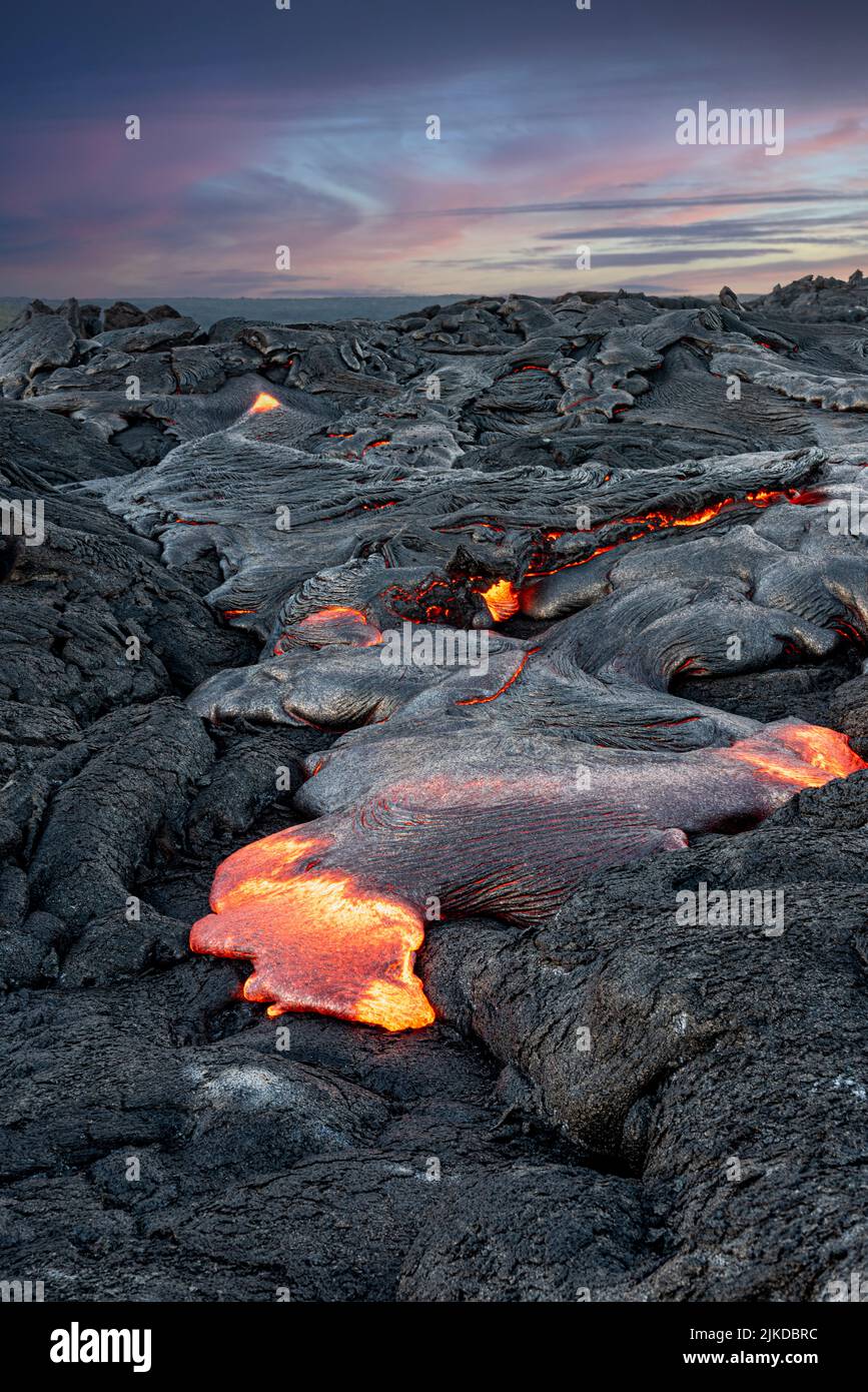 Lava en erupción al atardecer en Hawai rezuma a través de la corteza terrestre para formar nuevas rocas volcánicas. Foto de stock