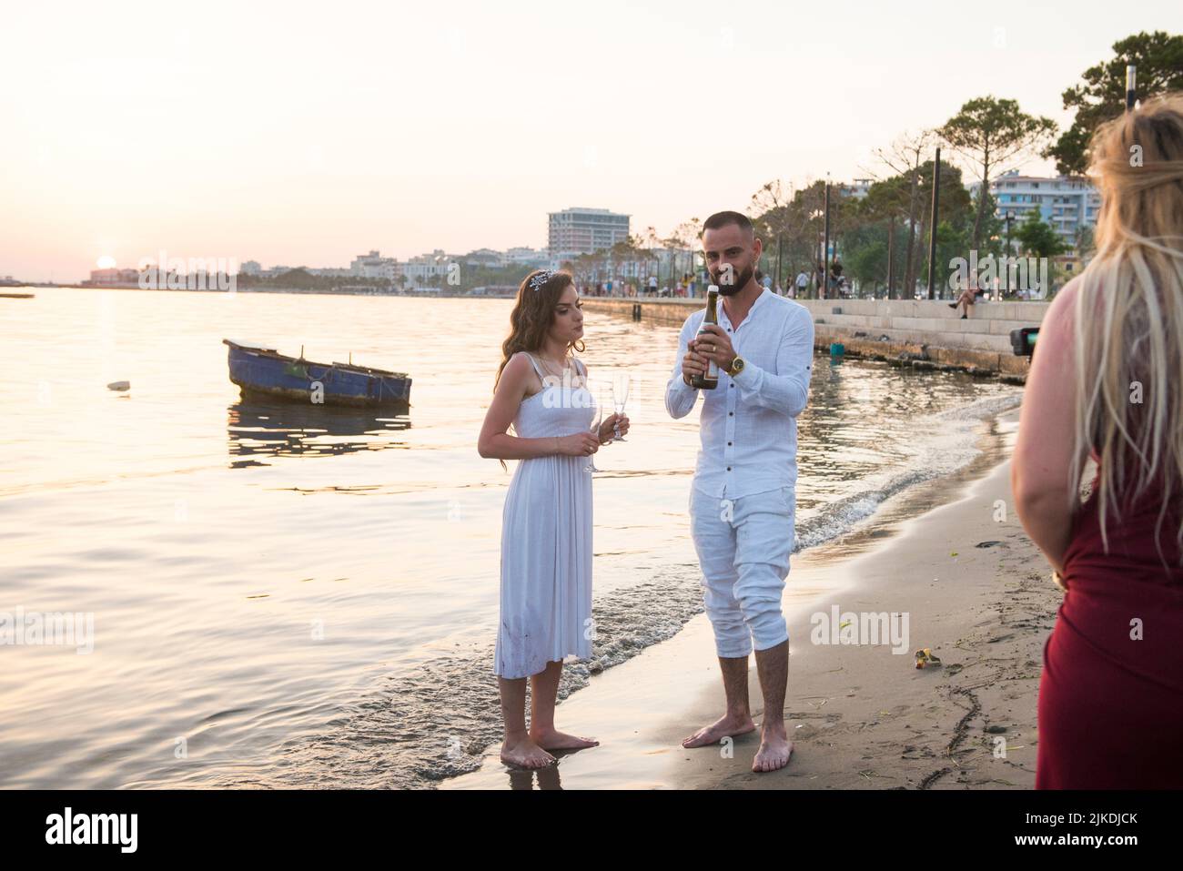 Un par de recién casados posando mientras bebían champán en la playa al atardecer. Promenade at Vlore, balneario en el mar Adriático, Albania, Foto de stock