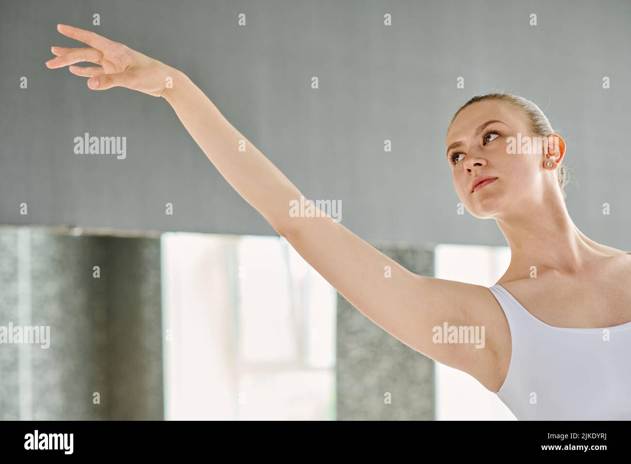 Joven bailarina elegante con brazo extendido mirando hacia adelante durante la actuación en el escenario o la repetición en el aula Foto de stock