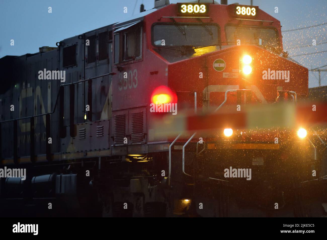 Bartlett, Illinois, EE.UU. Una locomotora Canadian National Railway conduce un tren de carga más allá de una puerta de paso de grado en una noche empapada de lluvia. Foto de stock