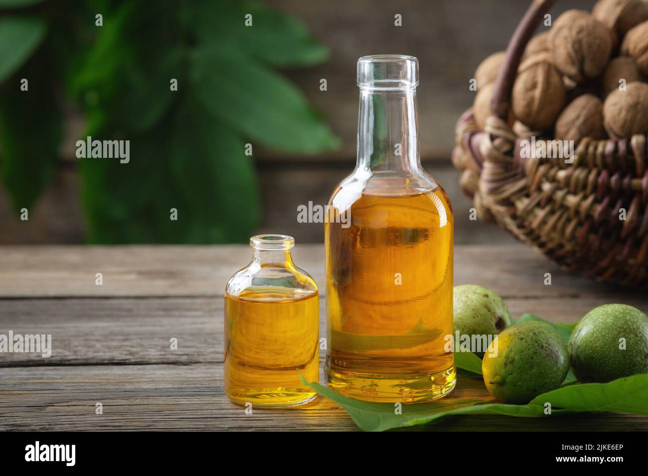 Botellas de aceite esencial de nuez, nueces verdes y maduras. Cesta de frutos secos en el fondo. Foto de stock