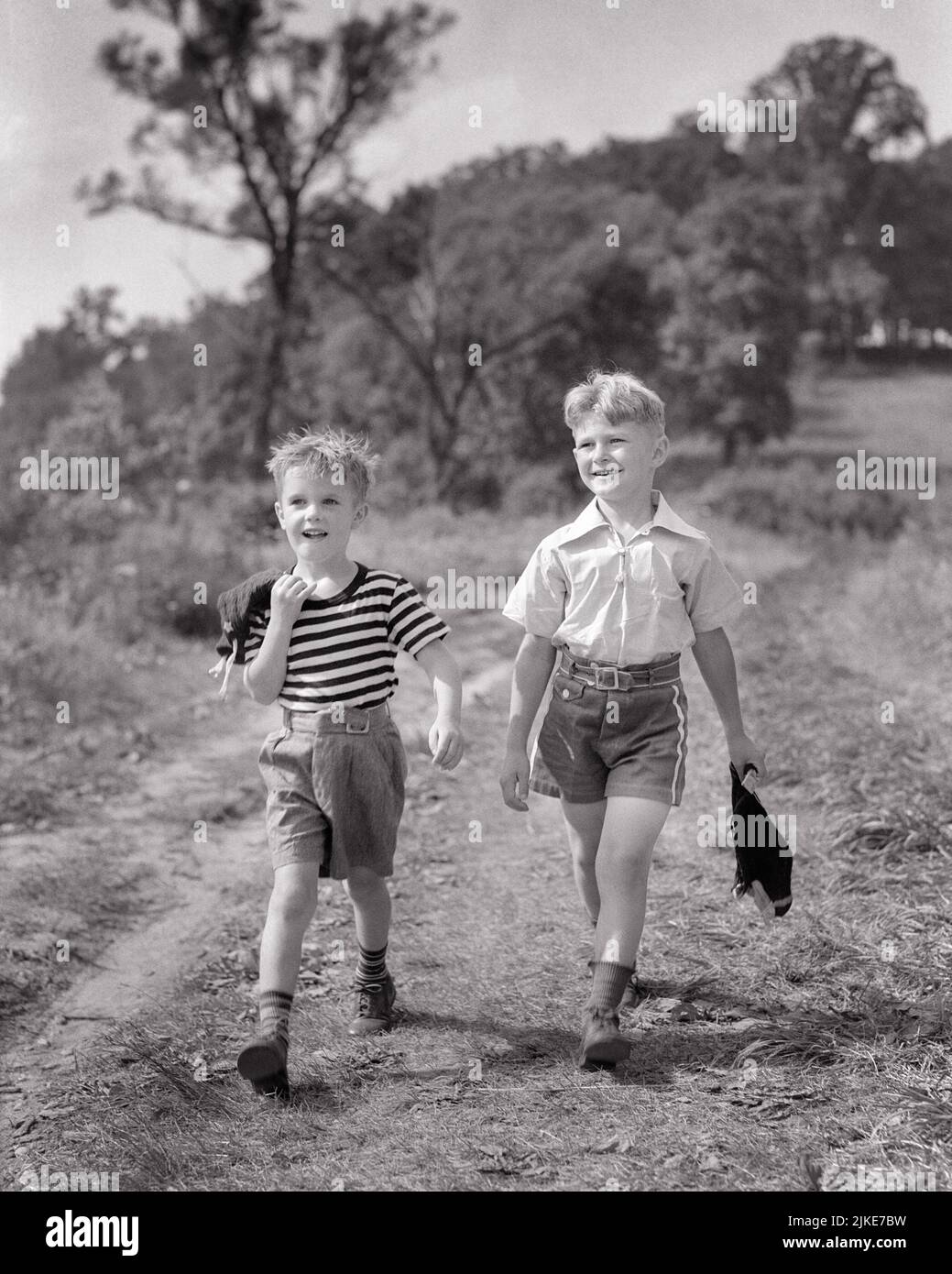 1930S DOS NIÑOS SONRIENTES QUE LLEVABAN PANTALONES CORTOS CAMINANDO POR EL  CAMPO CON EL PELO MOJADO SUJETANDO BAÑADORES HÚMEDOS - J1415 HAR001 HARS  ALEGRÍA ESTILO DE VIDA SATISFACCIÓN HERMANOS RURALES SALUD HOGAR