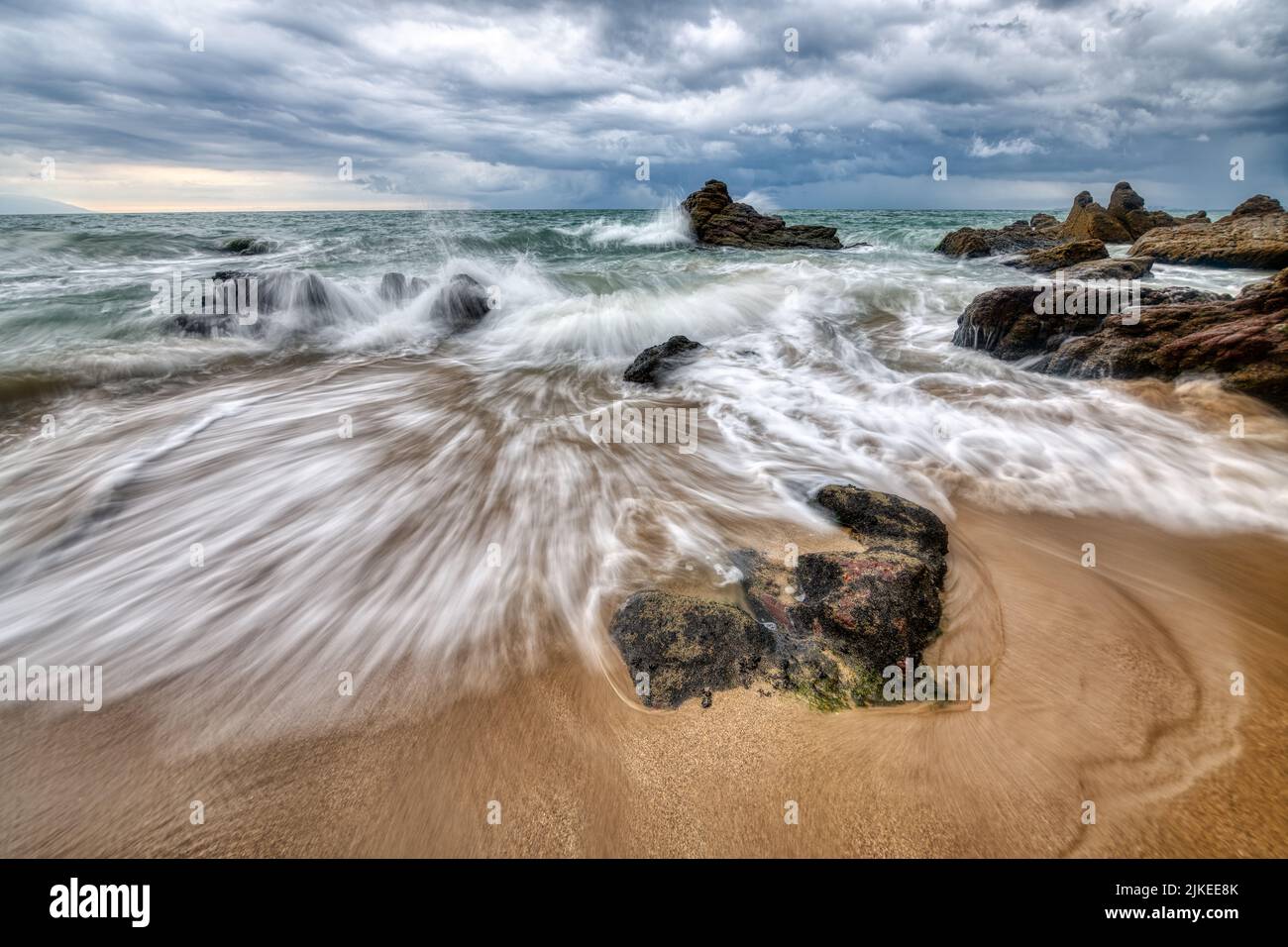 Una ola del océano está rompiendo en Una playa tropical contra Un colorido cielo al atardecer Foto de stock