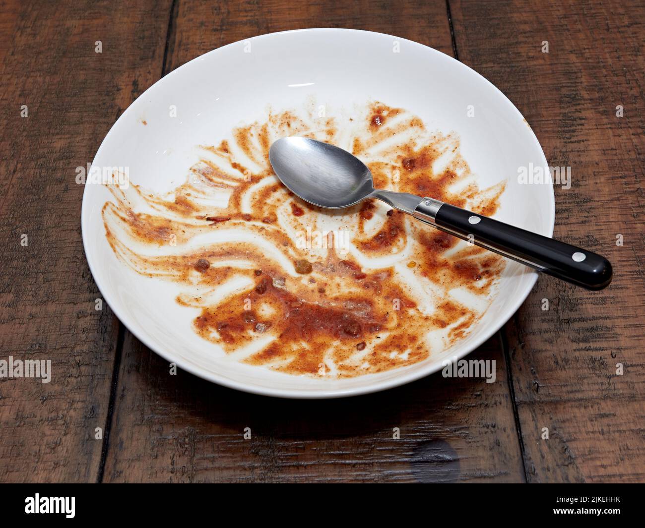 Vacíe el cuenco blanco sucio y coloque una cuchara sobre una mesa de madera después de una comida de chile o sopa espesa. Foto de stock