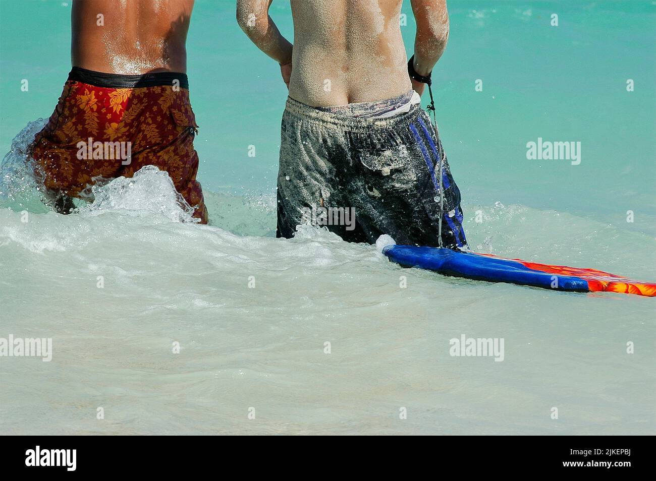 Vista trasera de dos niños mexicanos entrando al mar con arena en los cuerpos de su traje de baño Foto de stock