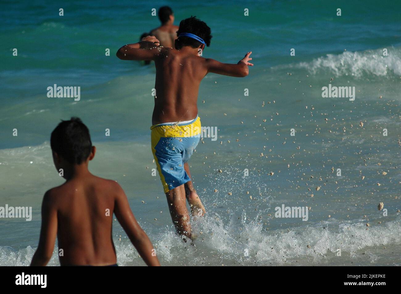 Vista trasera en un joven mexicano corriendo en el mar, y saltando sobre las olas. Enfoque selectivo Foto de stock