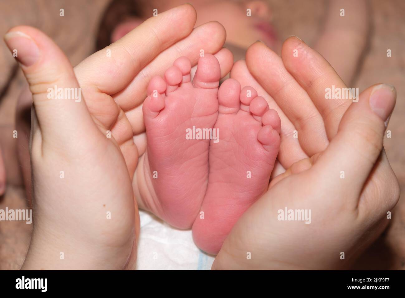 Las piernas de un bebé de dos semanas de edad están en manos de una madre. Las palmas de una mujer y los pies de un niño, el amor y el cuidado de los padres, la creación Foto de stock