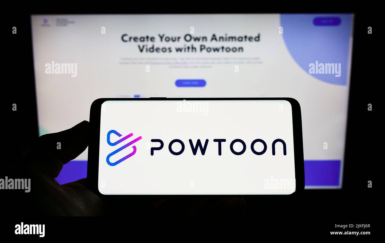 Persona que sostiene el smartphone con el logotipo de la compañía de software de animación Powtoon.com Inc. En la pantalla delante del sitio web. Enfoque la pantalla del teléfono. Foto de stock