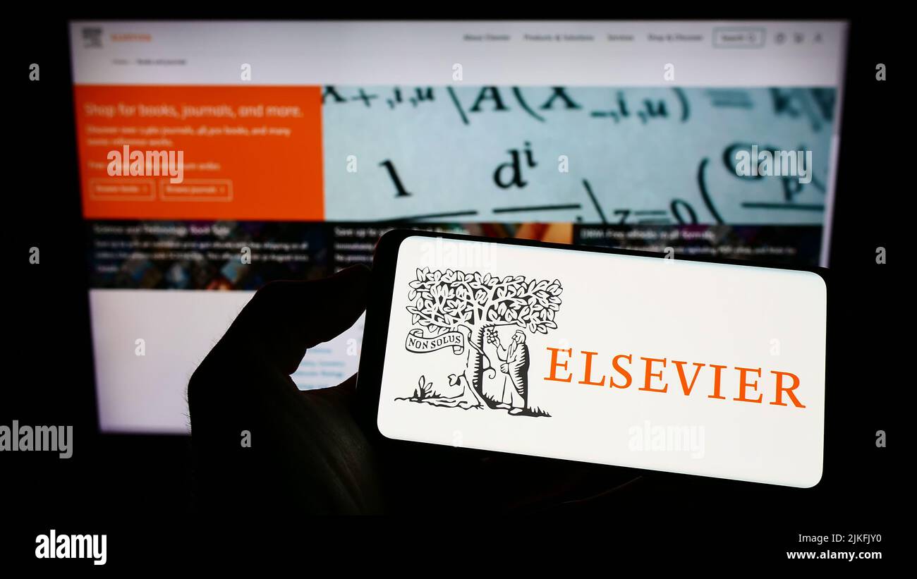 Persona que sostiene el teléfono móvil con el logotipo de la editorial académica Elsevier en la pantalla delante de la página web de negocios. Enfoque la pantalla del teléfono. Foto de stock