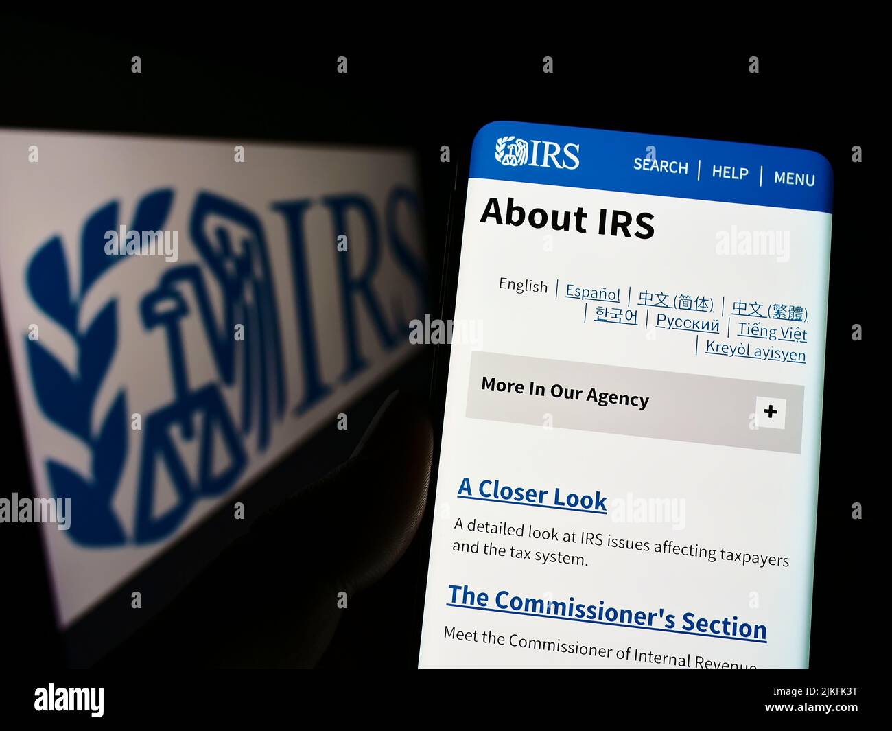 Persona que sostiene el teléfono celular con la página web de US Internal Revenue Service (IRS) en la pantalla delante del logotipo. Enfoque en el centro de la pantalla del teléfono. Foto de stock