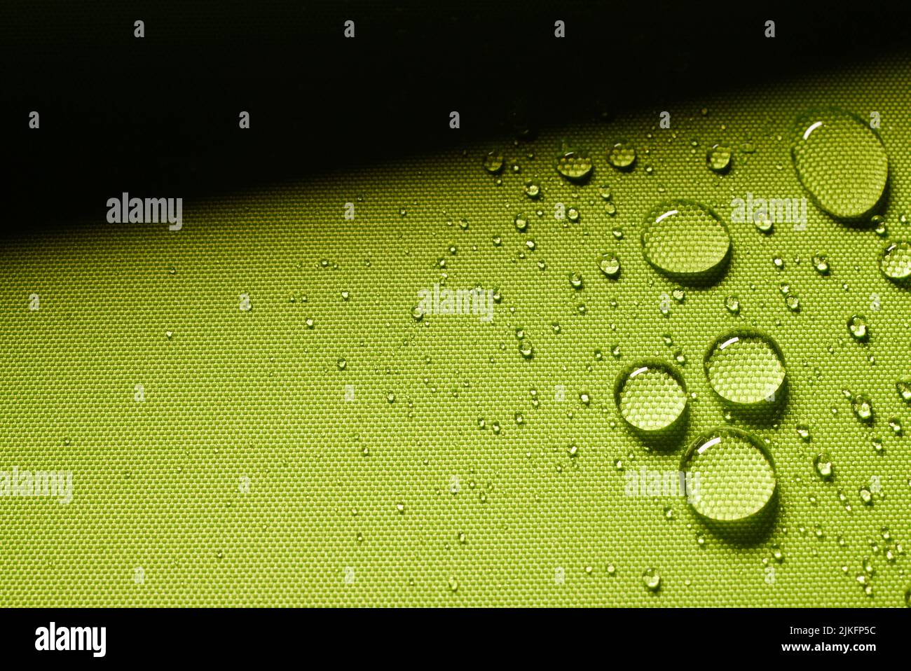 Vista superior de fondo verde abstracto con primer plano de gotas de agua sobre tela impermeable impregnada con sombra en habitación de luz Foto de stock